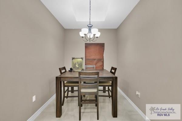dining space with baseboards, a raised ceiling, and an inviting chandelier