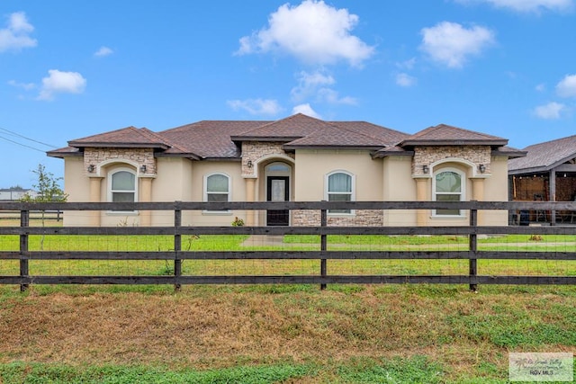 view of front of house featuring a front yard, stone siding, a fenced front yard, and stucco siding