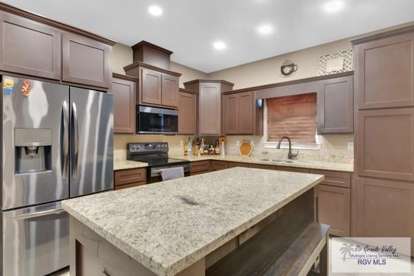 kitchen featuring light stone counters, recessed lighting, a sink, appliances with stainless steel finishes, and a center island