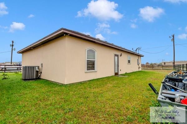 view of home's exterior with stucco siding, a lawn, central AC unit, and fence