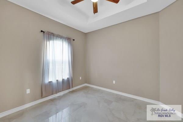 empty room featuring a tray ceiling, baseboards, and ceiling fan