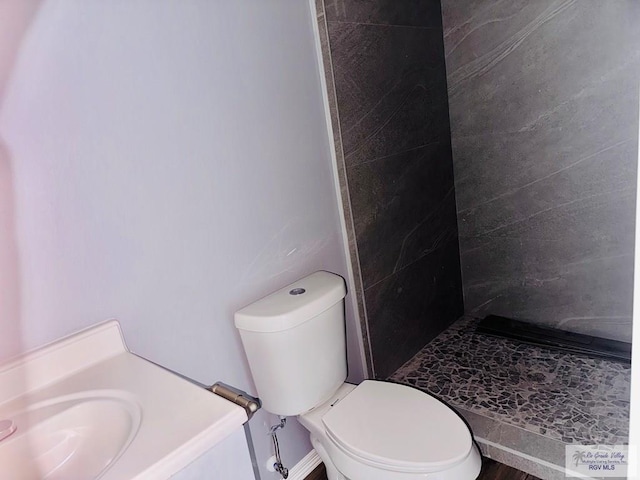 bathroom with tiled shower, sink, and toilet