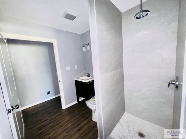 bathroom with hardwood / wood-style floors, vanity, toilet, and a tile shower