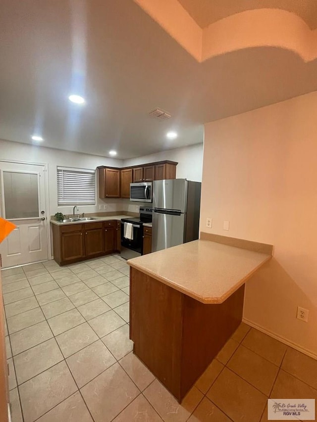 kitchen with light tile patterned floors, kitchen peninsula, sink, and appliances with stainless steel finishes