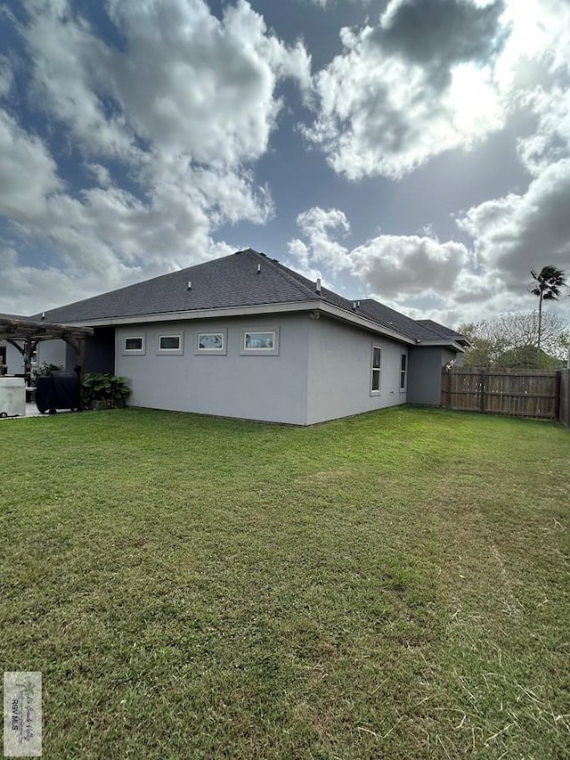 back of property with stucco siding, a lawn, and fence