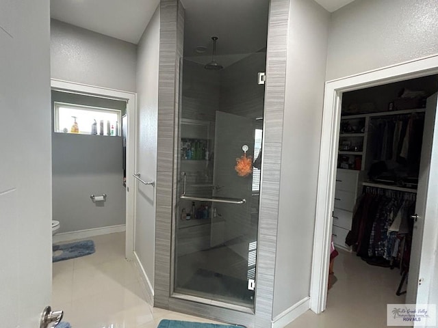 bathroom with toilet, baseboards, a spacious closet, tile patterned floors, and a stall shower