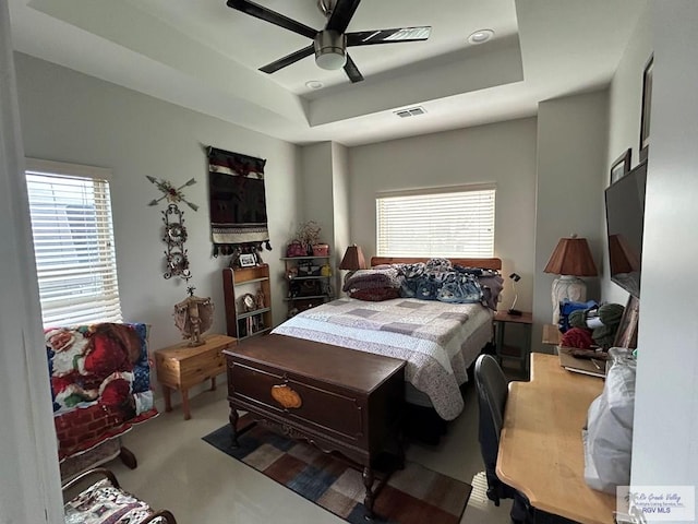 bedroom with ceiling fan, multiple windows, visible vents, and a raised ceiling