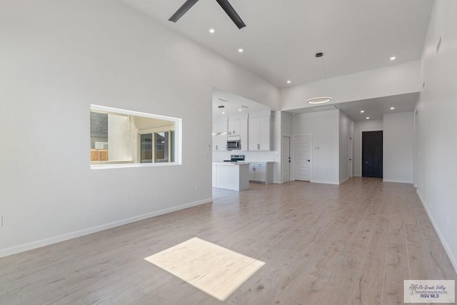 unfurnished living room with a high ceiling, ceiling fan, and light hardwood / wood-style flooring