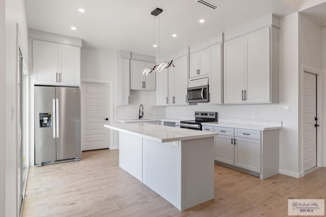 kitchen featuring sink, a center island, light wood-type flooring, appliances with stainless steel finishes, and pendant lighting