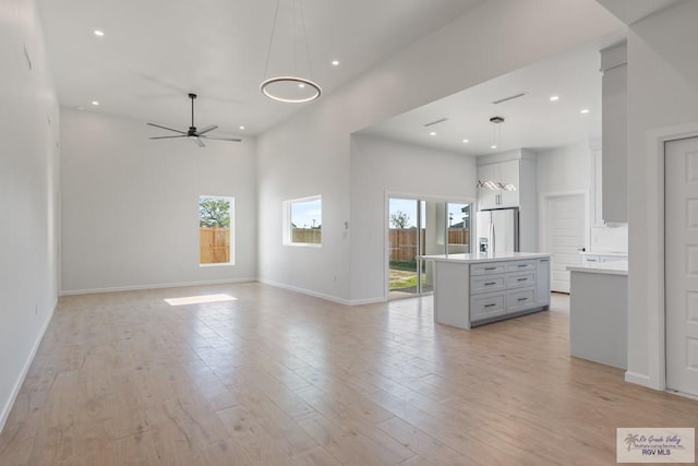 unfurnished living room featuring a towering ceiling, a wealth of natural light, ceiling fan, and light hardwood / wood-style flooring