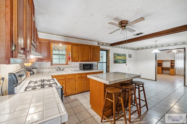 734 Billy Mitchell Blvd, Brownsville, TX 78521 - kitchen featuring tile countertops, black microwave, ceiling fan, white range with gas cooktop, and a center island