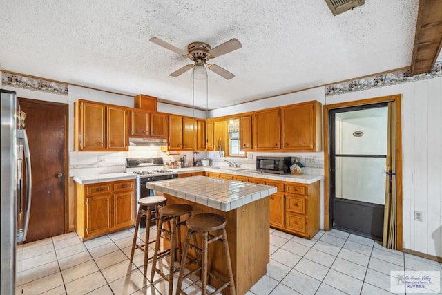 734 Billy Mitchell Blvd, Brownsville, TX 78521 - kitchen featuring tile counters, appliances with stainless steel finishes, under cabinet range hood, a sink, and a textured ceiling