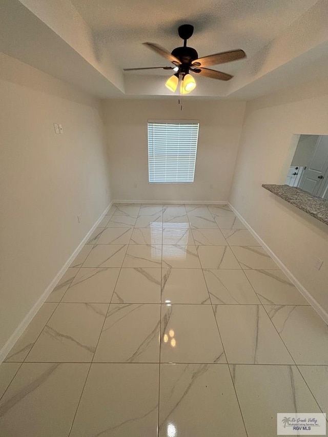 unfurnished room featuring ceiling fan, a textured ceiling, and a tray ceiling