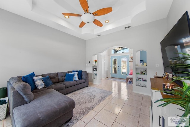 living room featuring a tray ceiling, ceiling fan, french doors, and light tile patterned flooring