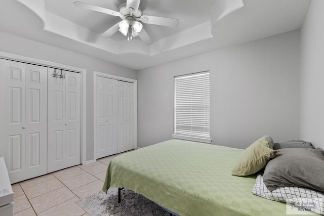 bedroom featuring a tray ceiling, multiple closets, ceiling fan, and light tile patterned flooring