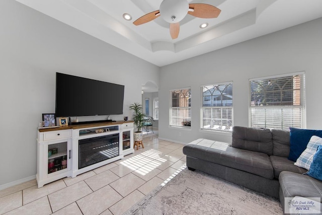 living room with a tray ceiling, ceiling fan, a towering ceiling, and light tile patterned floors