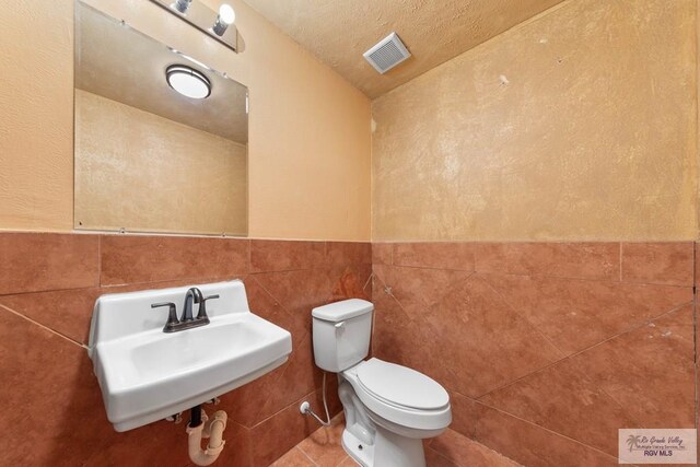 2307 Carlos Ave, Brownsville, TX 78526 - half bath with toilet, a wainscoted wall, a sink, visible vents, and tile walls