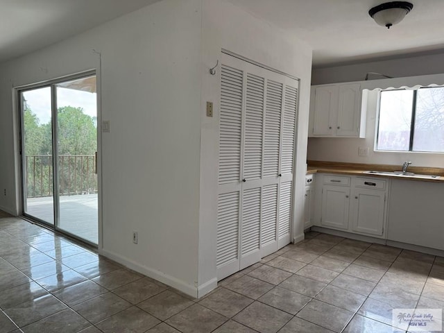 kitchen with light tile patterned floors, sink, and white cabinets