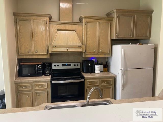 kitchen with tasteful backsplash, premium range hood, stainless steel range with electric stovetop, sink, and white fridge