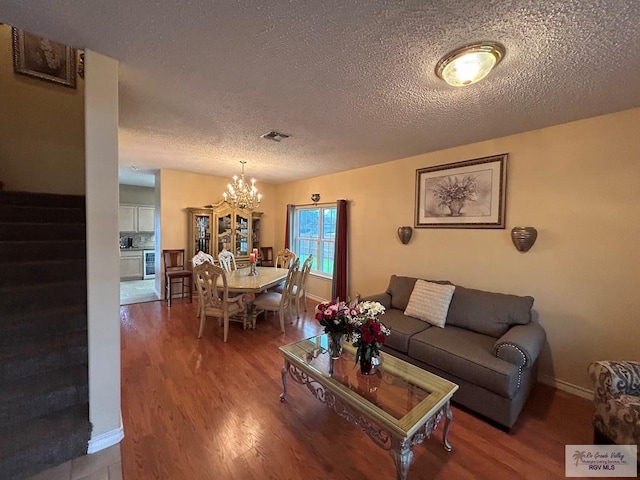 living room featuring wine cooler, hardwood / wood-style floors, a notable chandelier, and a textured ceiling