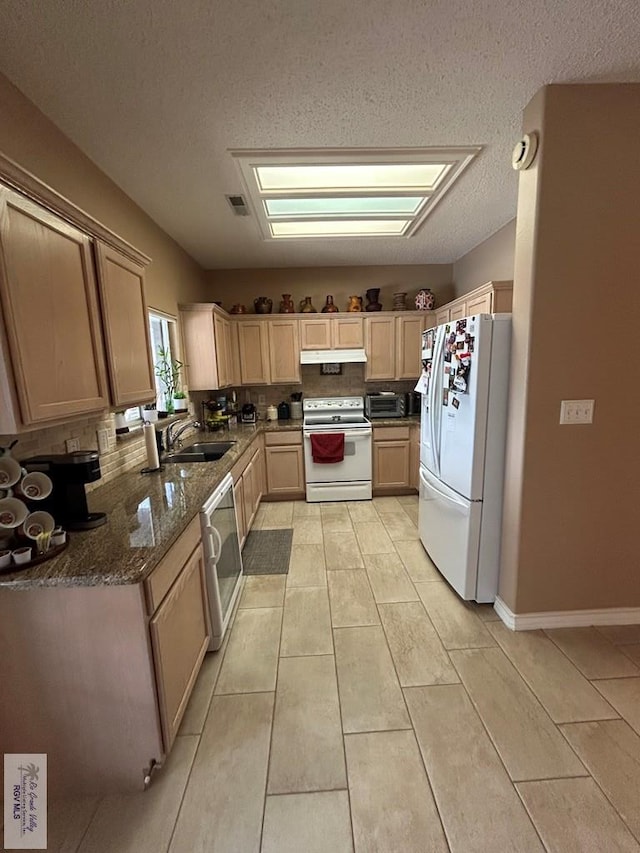 kitchen with light brown cabinetry, sink, white appliances, and dark stone counters