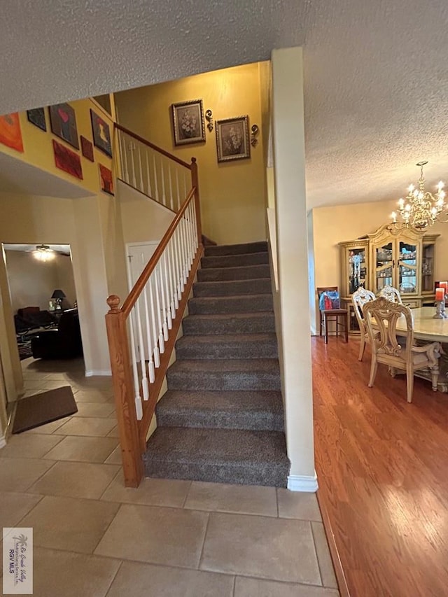 stairway featuring an inviting chandelier and a textured ceiling