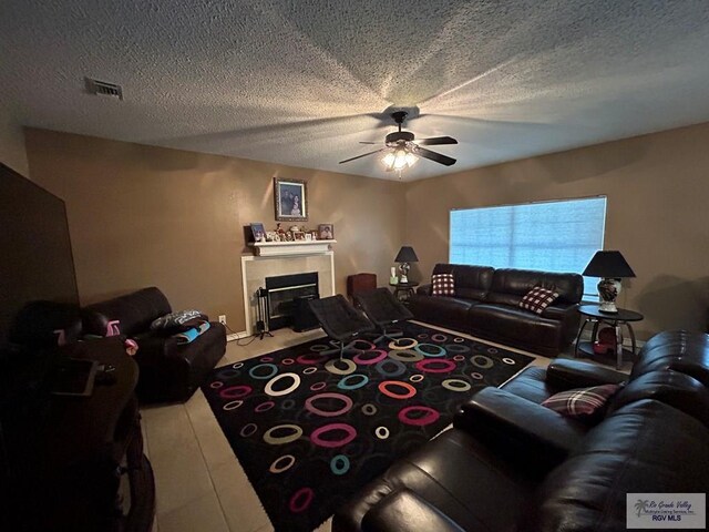 living room featuring a tiled fireplace, a textured ceiling, and ceiling fan