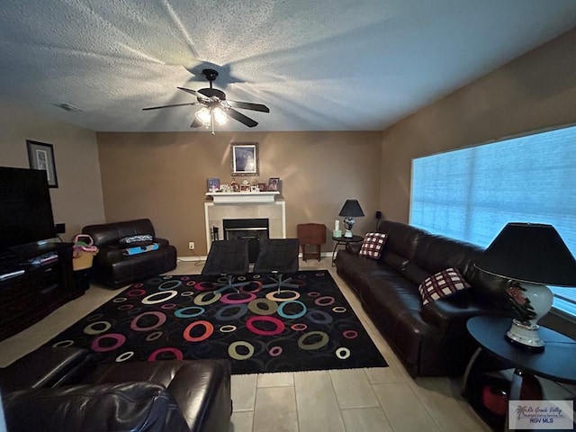 living room featuring a tiled fireplace, ceiling fan, and a textured ceiling