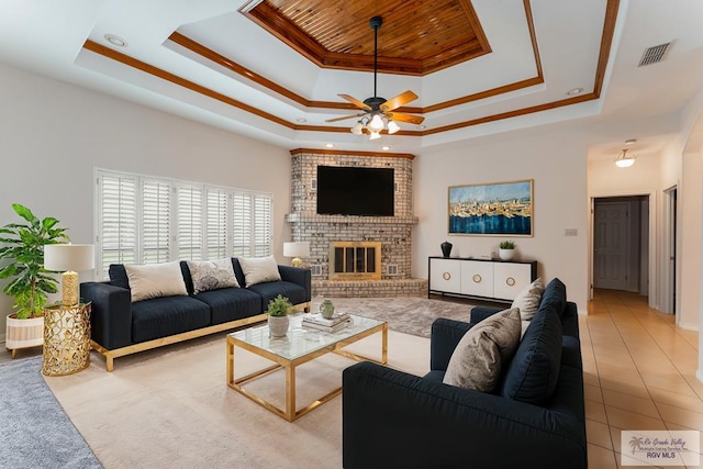 tiled living room featuring ceiling fan, a fireplace, a tray ceiling, and crown molding