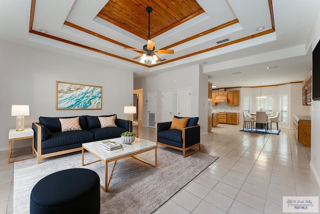 tiled living room with a raised ceiling, ornamental molding, and ceiling fan with notable chandelier