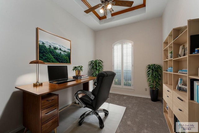 carpeted office featuring a raised ceiling and ceiling fan