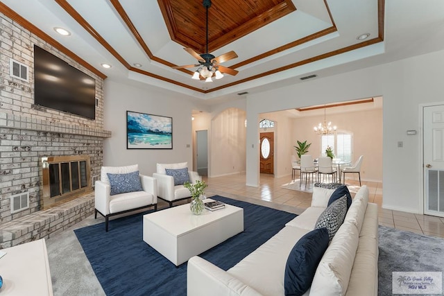 tiled living room featuring a tray ceiling, a fireplace, ornamental molding, and ceiling fan with notable chandelier