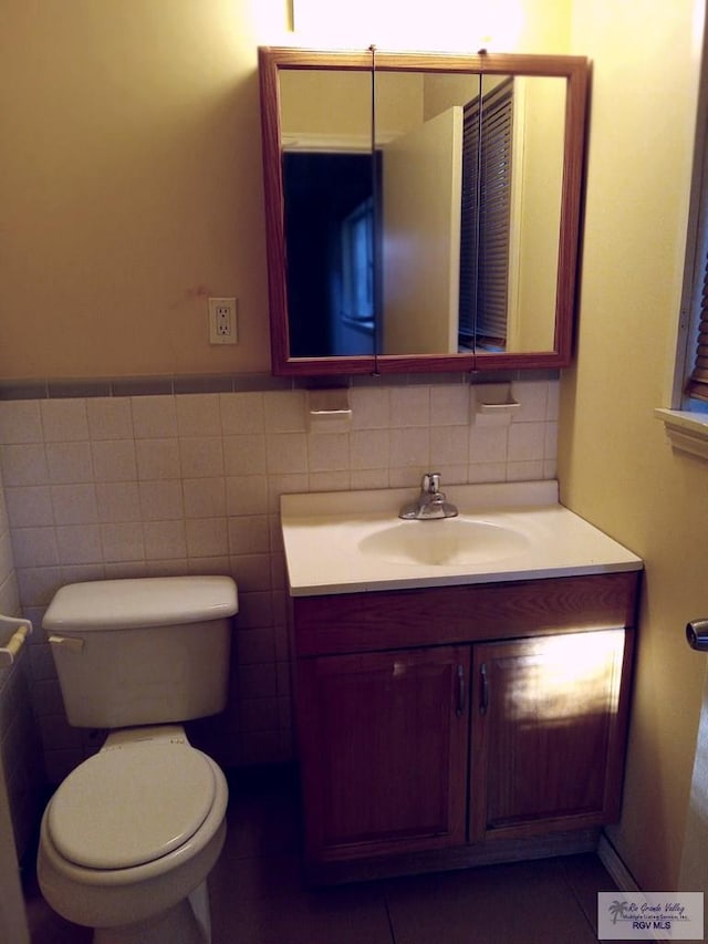 bathroom featuring toilet, vanity, tile patterned floors, and tile walls