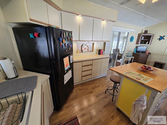 kitchen featuring white cabinetry, black refrigerator, hardwood / wood-style floors, and a breakfast bar area