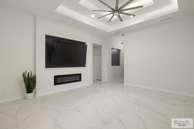 unfurnished living room featuring a tray ceiling, ceiling fan, and marble finish floor