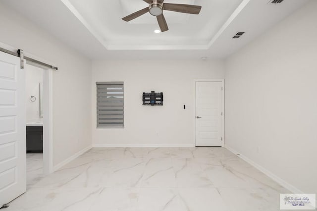 unfurnished room featuring a barn door, a raised ceiling, marble finish floor, a ceiling fan, and visible vents
