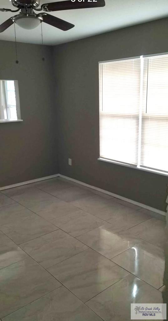 tiled empty room featuring baseboards and ceiling fan