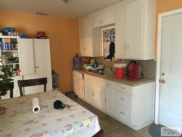 kitchen with tile patterned flooring, white cabinets, backsplash, and a sink