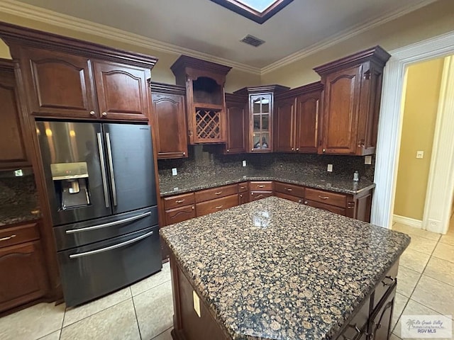 kitchen with dark stone countertops, stainless steel fridge, a kitchen island, and backsplash