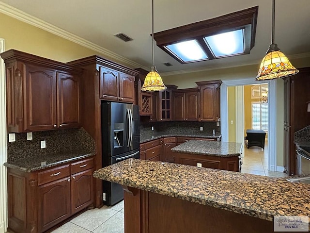 kitchen with dark stone counters, stainless steel fridge, a center island, and decorative light fixtures