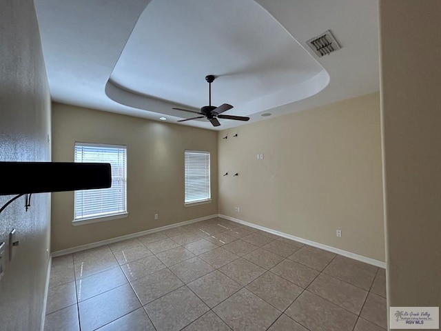 tiled spare room with ceiling fan and a tray ceiling