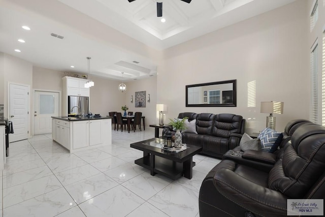 living room with ceiling fan, beam ceiling, a high ceiling, and coffered ceiling