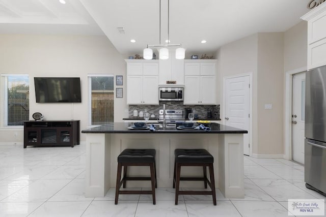 kitchen featuring white cabinetry, an island with sink, a breakfast bar area, decorative backsplash, and appliances with stainless steel finishes