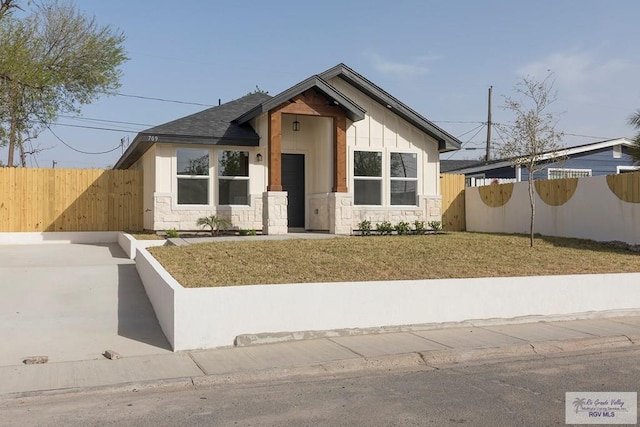 view of front facade featuring a front lawn, stone siding, and fence