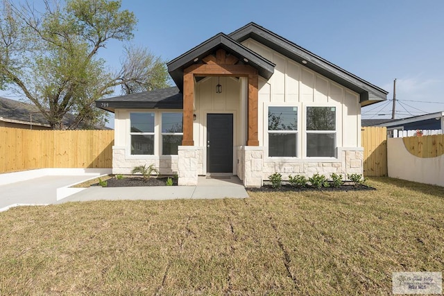 view of front facade with board and batten siding, a fenced backyard, a front yard, and stone siding