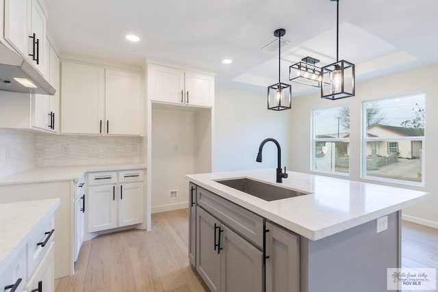 kitchen with decorative backsplash, a sink, a raised ceiling, recessed lighting, and light wood finished floors