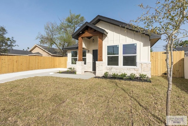 bungalow-style house featuring fence, a front lawn, and stone siding