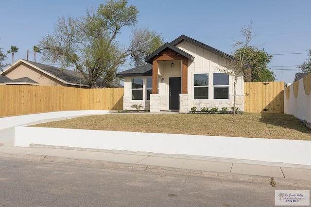 bungalow with a front yard, fence private yard, and stone siding