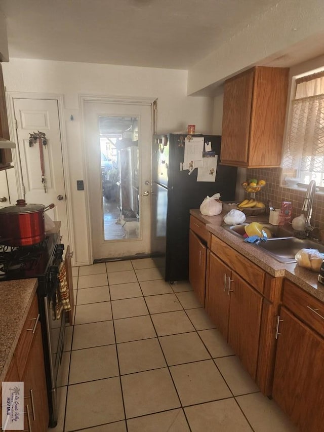 kitchen featuring decorative backsplash, black refrigerator, sink, light tile patterned floors, and stainless steel gas stove