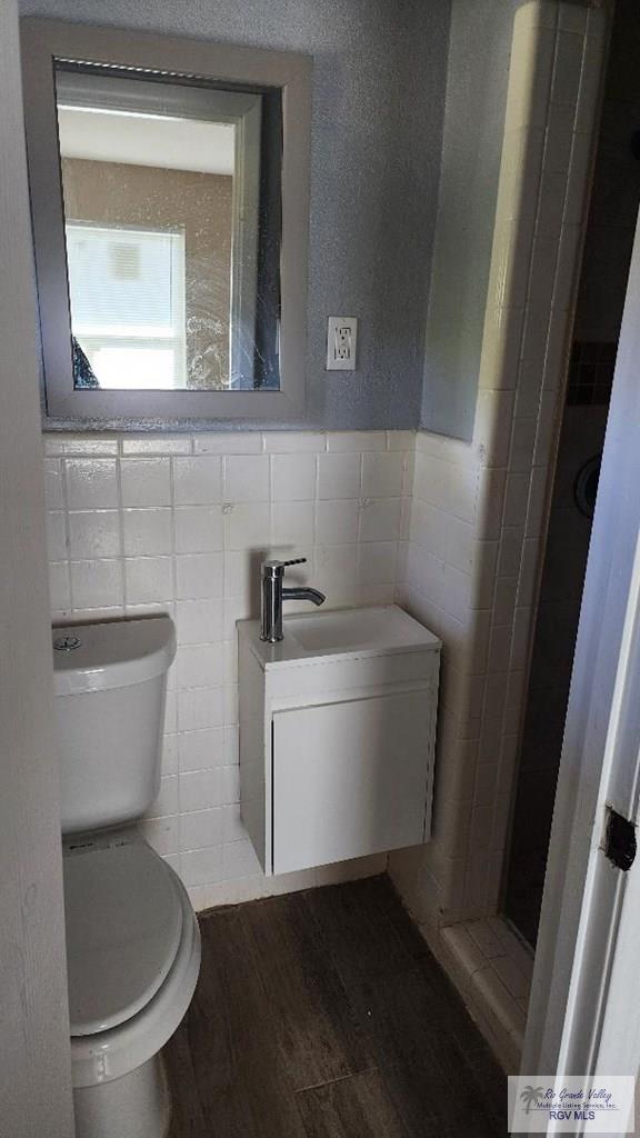 bathroom with hardwood / wood-style flooring, toilet, and tile walls